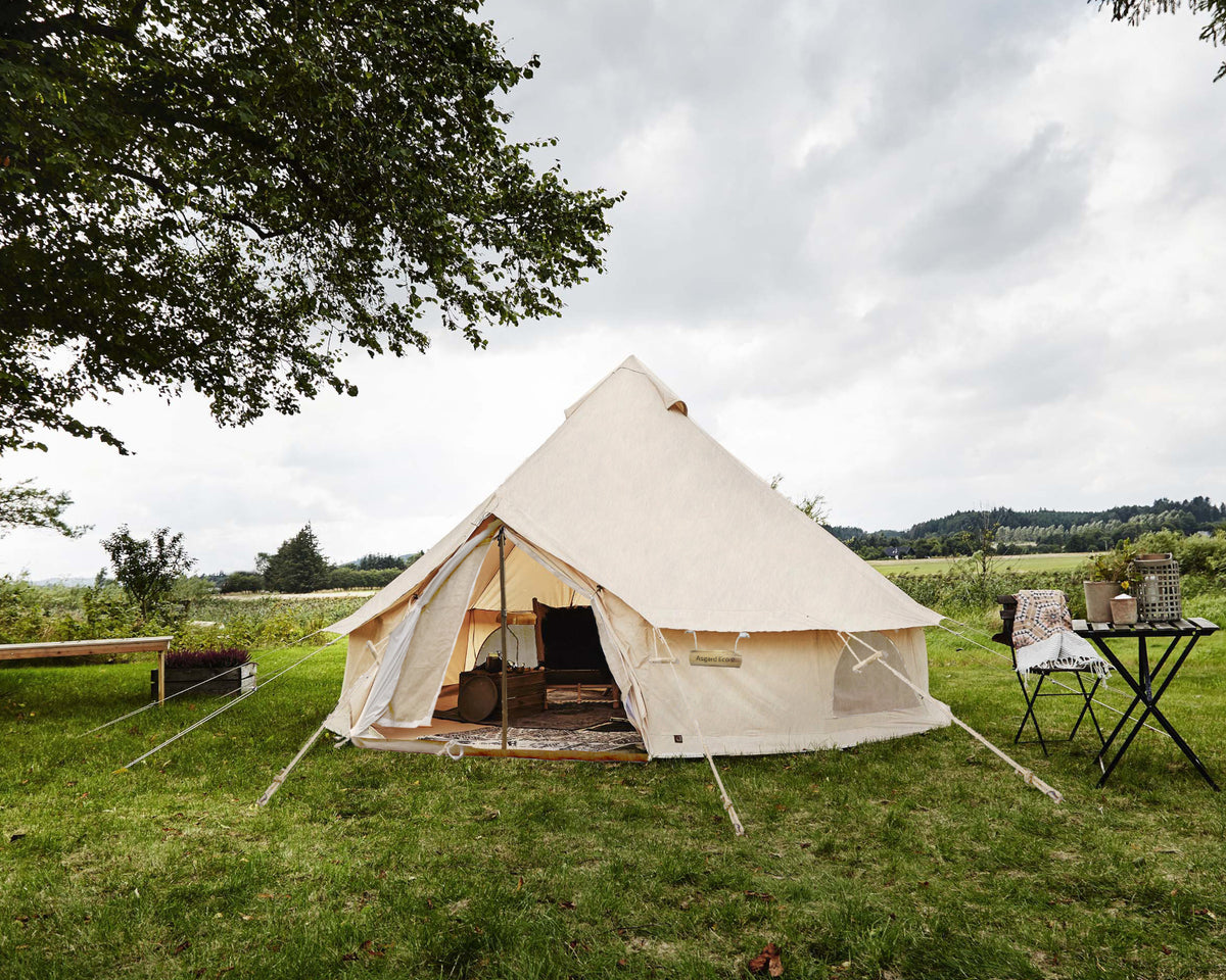 Beige bell tent in a grassy field with a cloudy sky