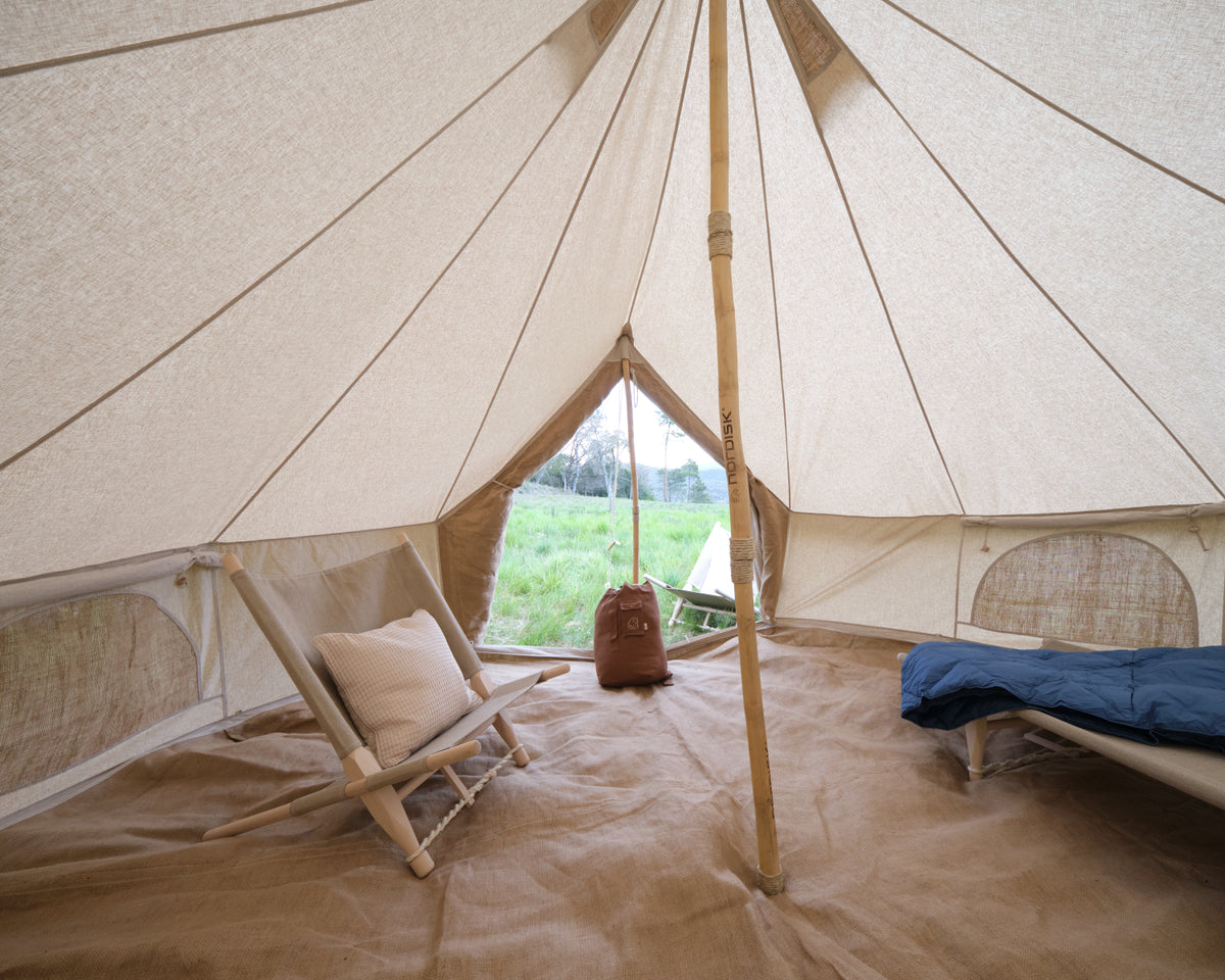 Interior of a large beige tent with a wooden chair, pillow, and sleeping bag.
