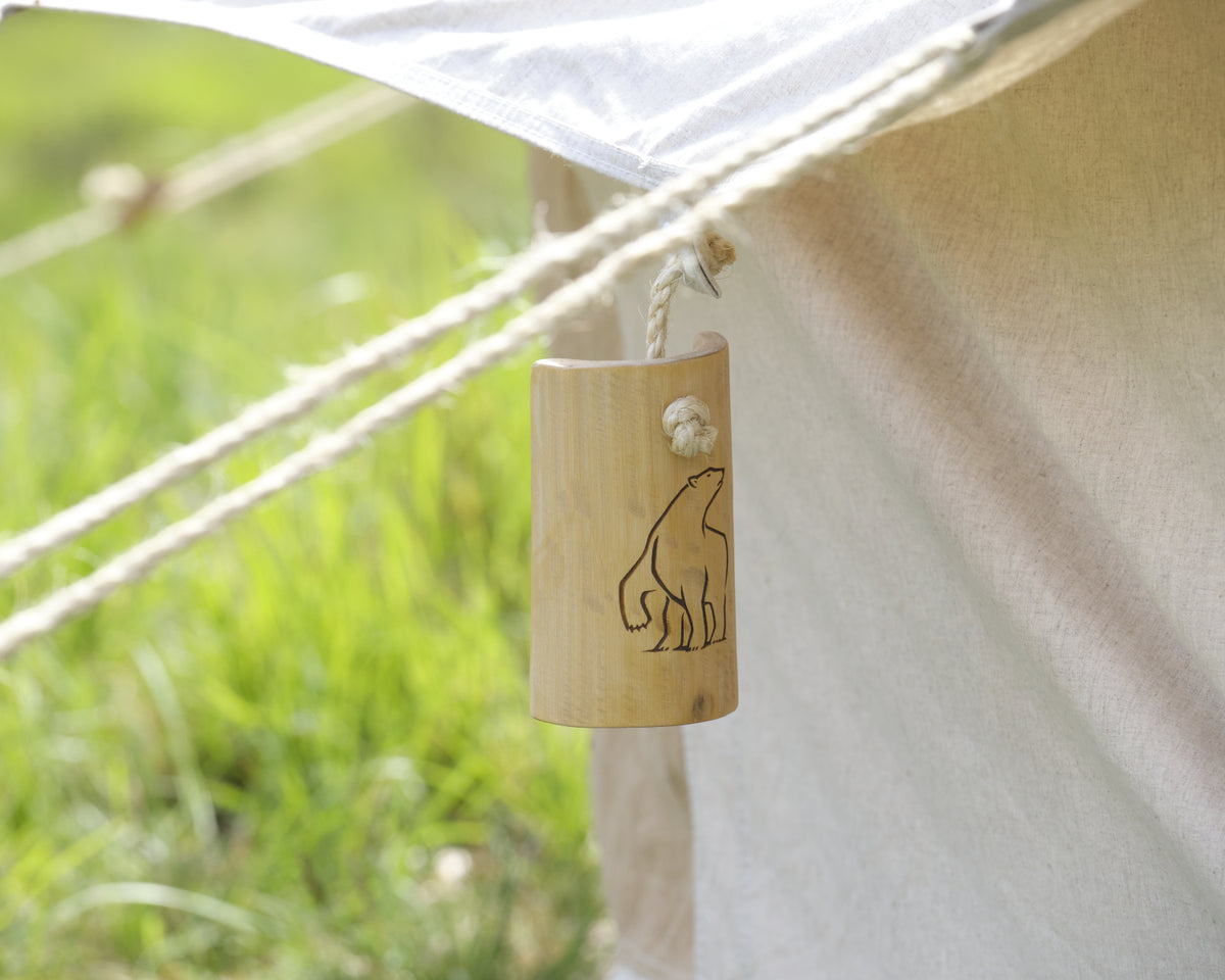 Wooden bell with bear design attached to a tent with grass in the background