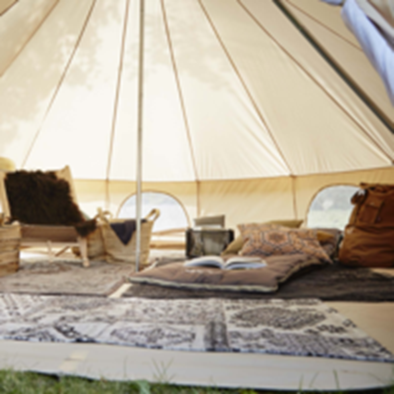 Interior view of a cozy Nordisk cotton tent set up for luxury glamping with rugs.