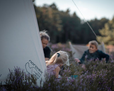 Nordisk cotton tarp category image showing people glamping in a field of purple flowers.