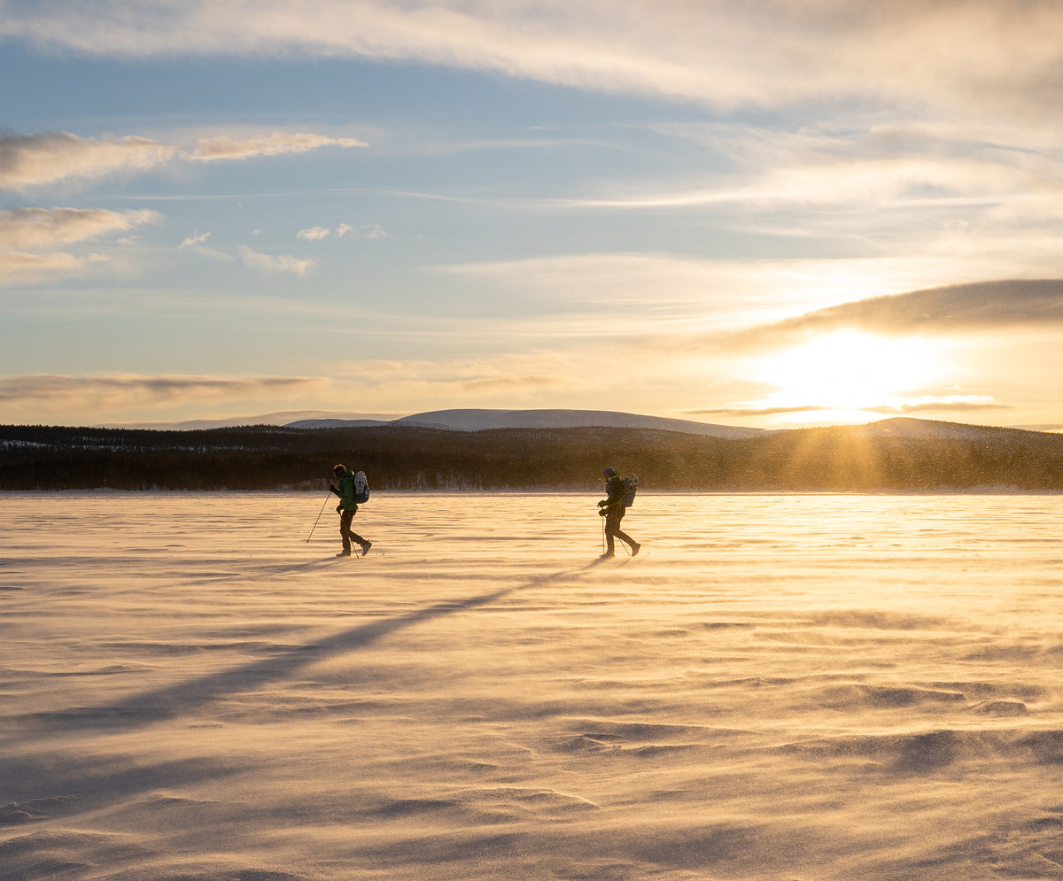 Two runners with backpacks trekking across a frozen snowy landscape during the Ice Ultra event.