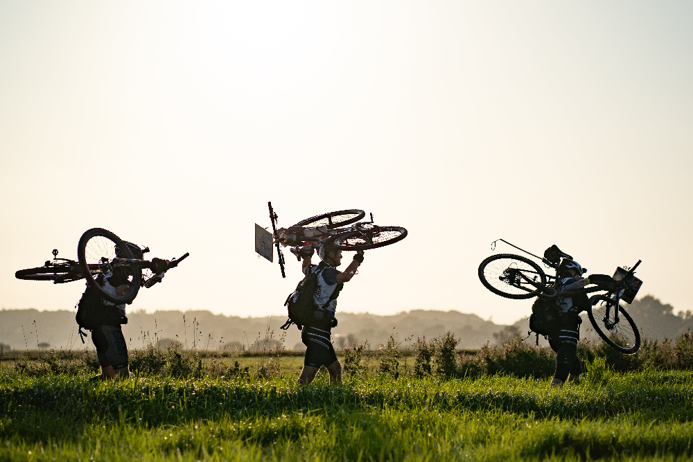 Participants carrying mountain bikes through a field during the Nordisk Adventure Challenge outdoor event.