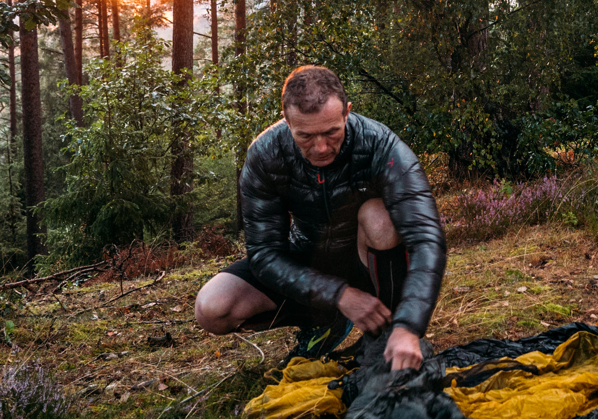 Man wearing the world's lightest down jacket packing a Nordisk tent in a forest.