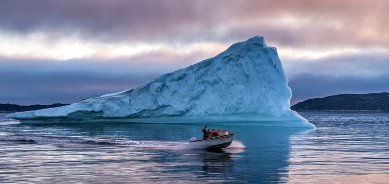 Small boat sailing past a large iceberg in Greenland during a glamping trip.