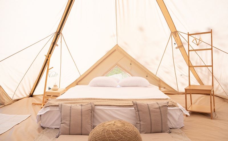 Interior of a luxury glamping tent in Thailand with a comfortable bed and wooden furniture.