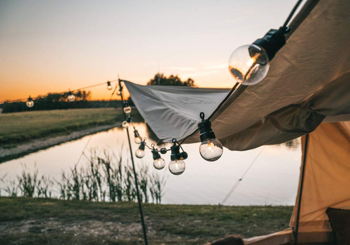 String lights and lanterns creating a hygge atmosphere outside a Nordisk glamping tent at sunset.