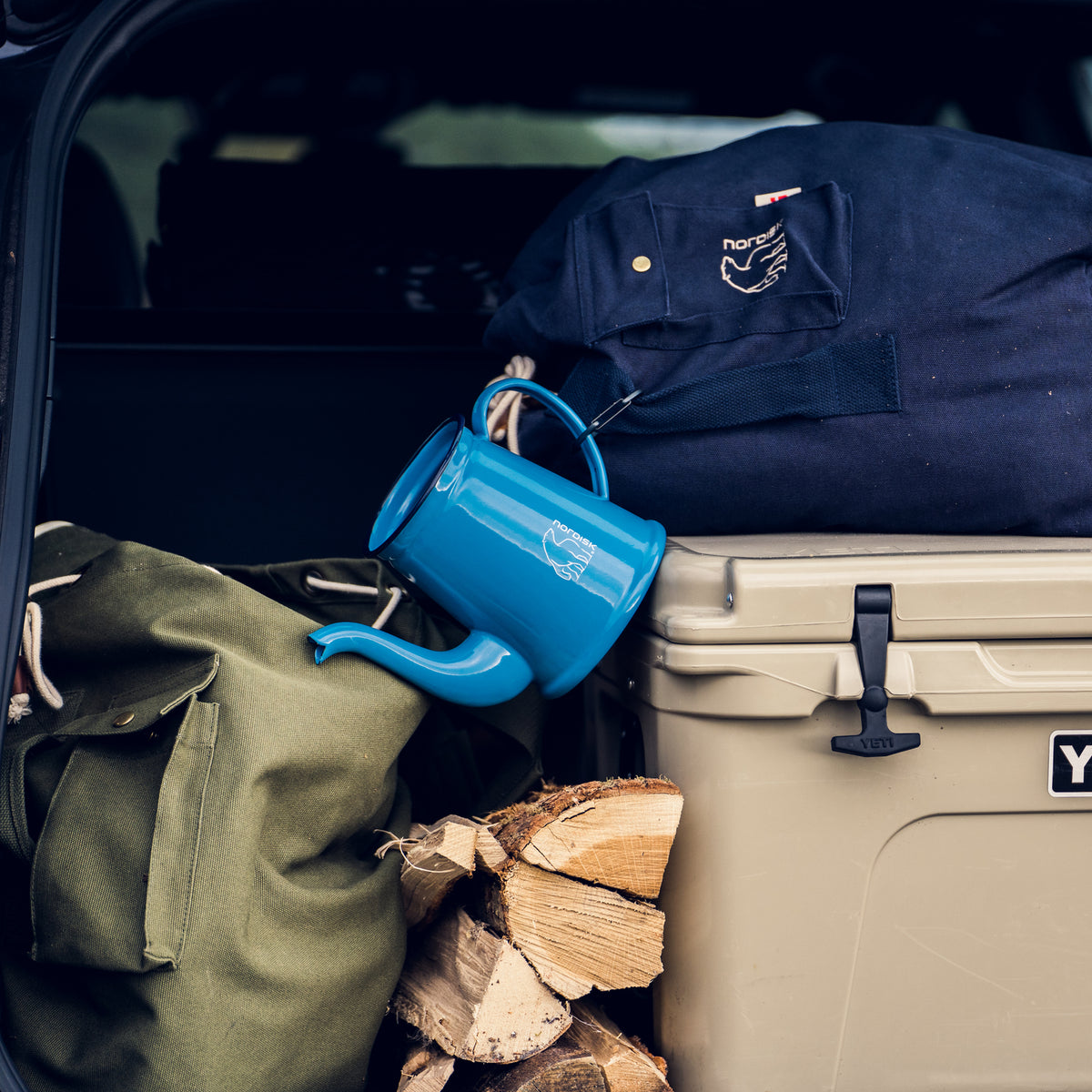 Nordisk glamping gear, including a blue kettle and luggage, packed in a car for outdoors.