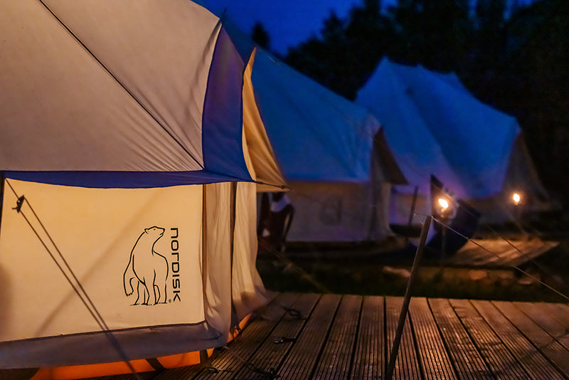 Illuminated Nordisk cotton glamping tents on a wooden deck at dusk in Germany.