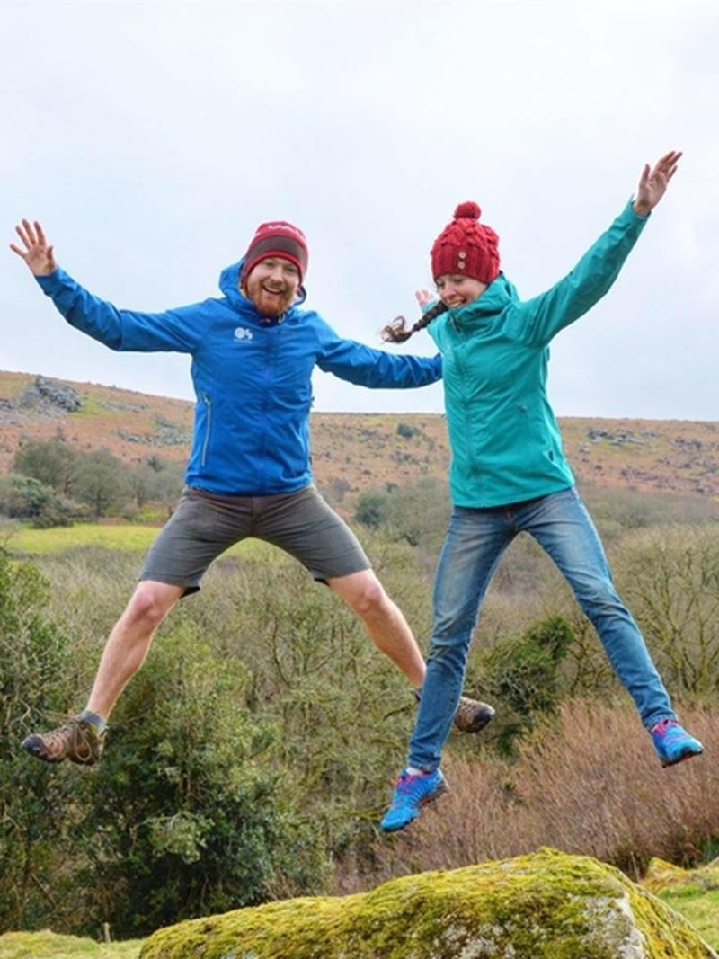 Nordisk Heroes Jen and Sim Benson jumping outdoors while wearing hiking gear.