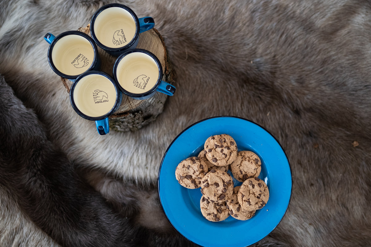 Blue Madam Blå enamel mugs and a plate with chocolate chip cookies on fur.