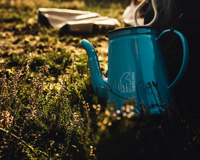 Blue Nordisk Madam Blå enamel coffee pot on a grassy outdoor camping background.