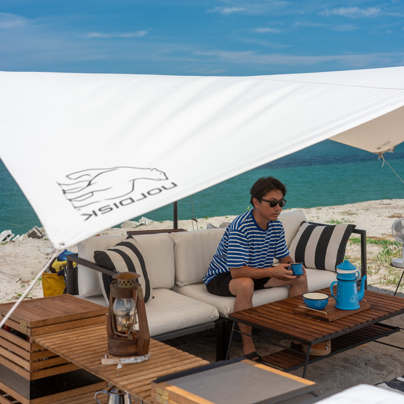 A man relaxing under a Nordisk tarp at the Muuu camp beach setup.
