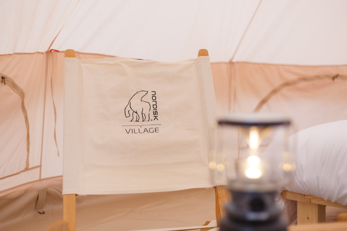 Canvas chair with Nordisk Village logo inside a luxury glamping tent with a lantern.