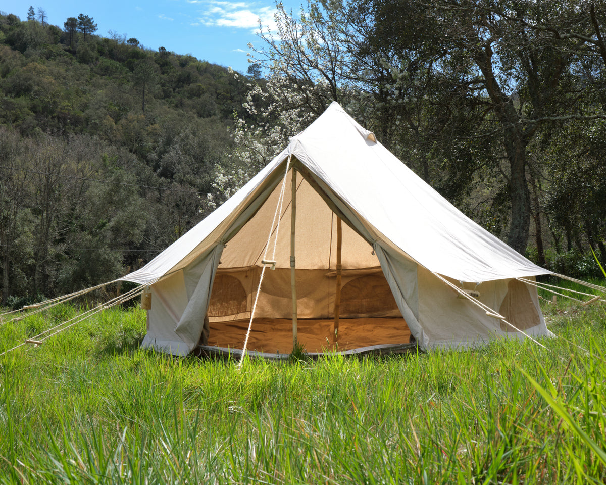 Beige bell tent in a grassy area with trees in the background