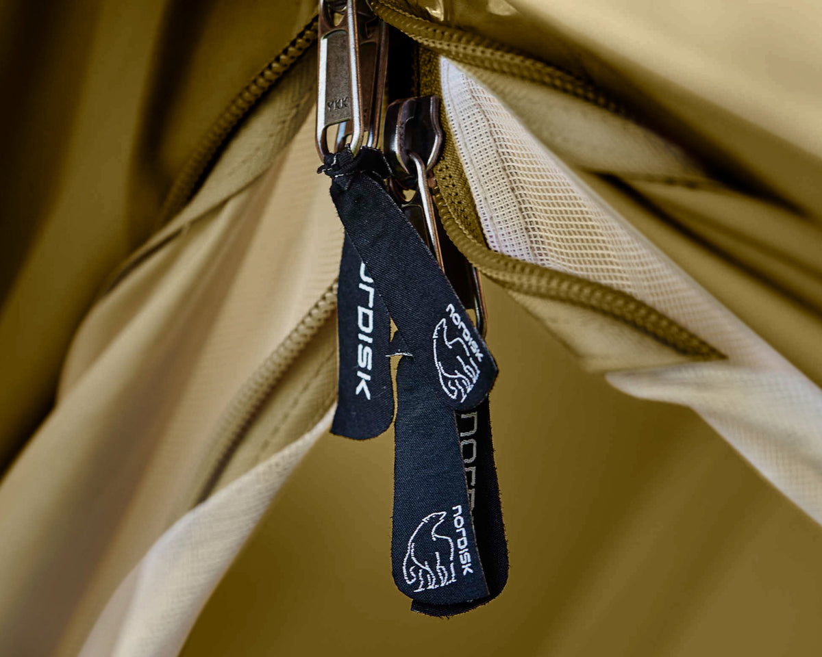 Close-up of a keychain with a brand logo attached to a beige bag.