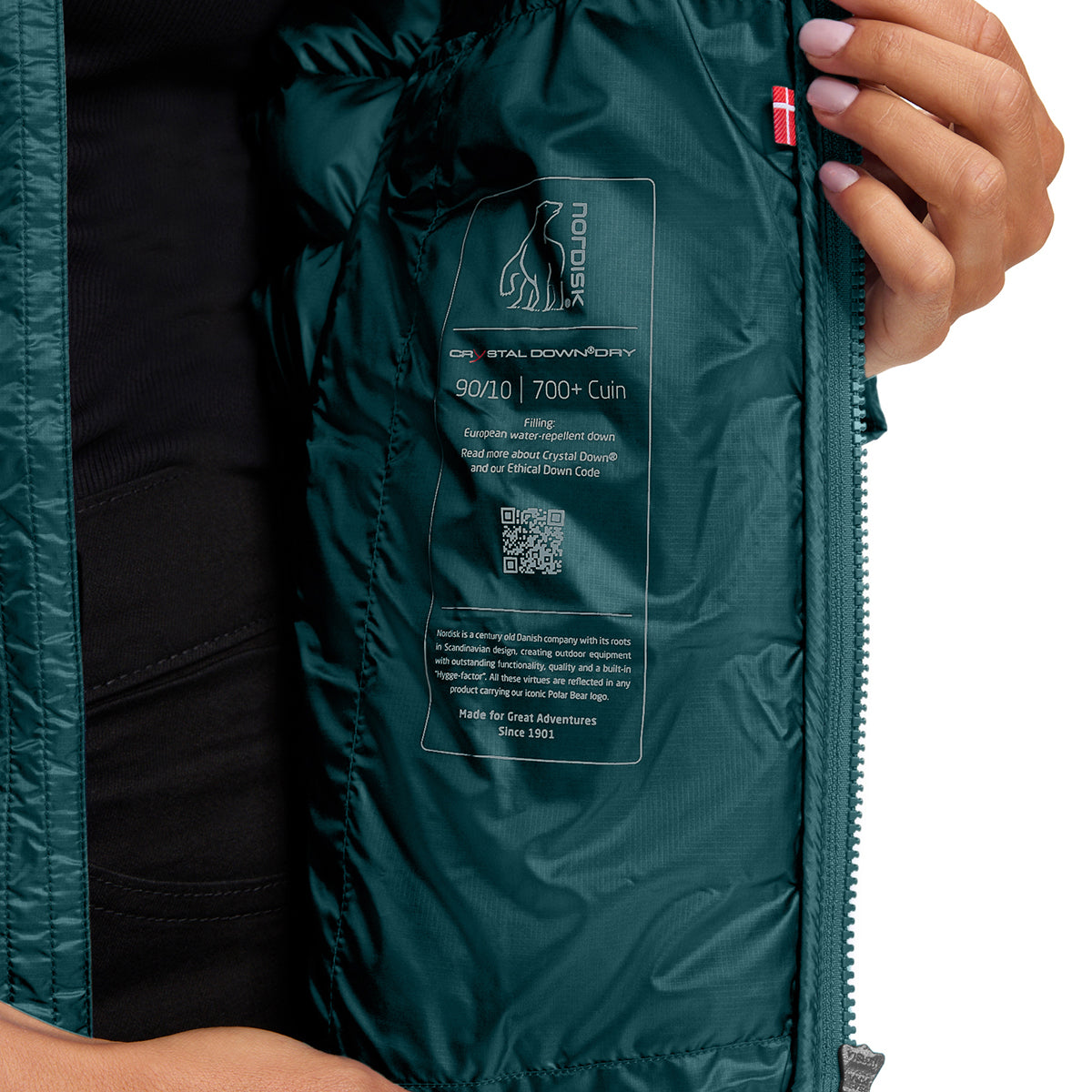 Close-up of a person opening a dark teal puffer jacket to show the inner lining with a printed label for Orion Original Down/Down-Ary 90/10 | 700+ Cuin.