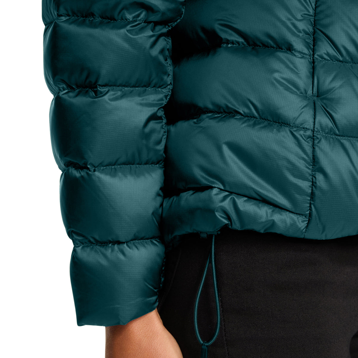 Close-up of a dark teal puffer jacket with horizontal quilting, worn by a model with black bottoms against a white background.