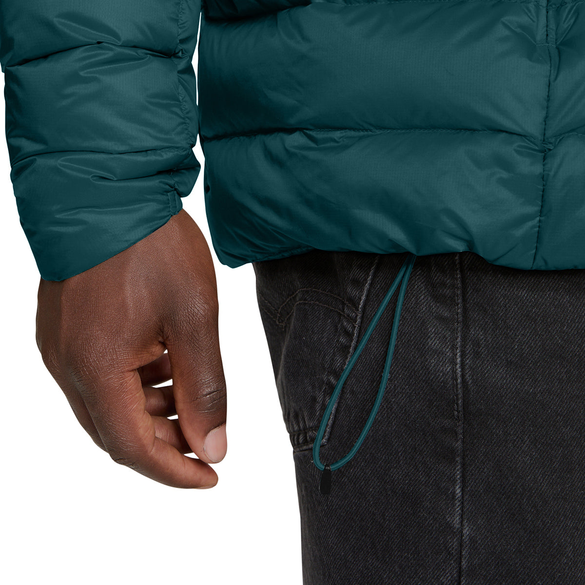 Close-up of a person wearing a dark teal puffer jacket and dark gray jeans, showing the sleeve, hand, and drawstring waist area against a white background.