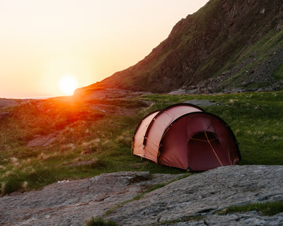 Red Nordisk tunnel tent pitched on a rocky mountain landscape during a golden sunset.