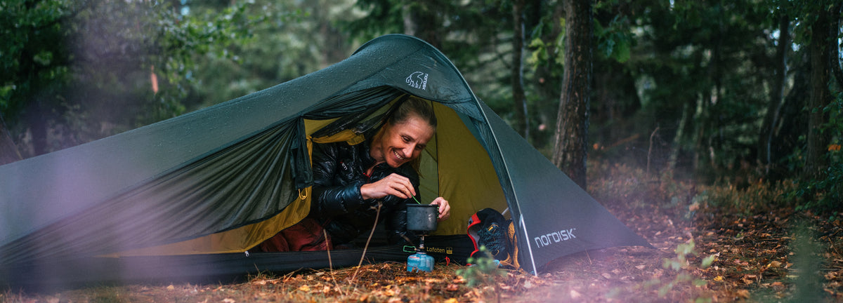 Woman cooking inside a lightweight Nordisk Lofoten tent in a forest setting.