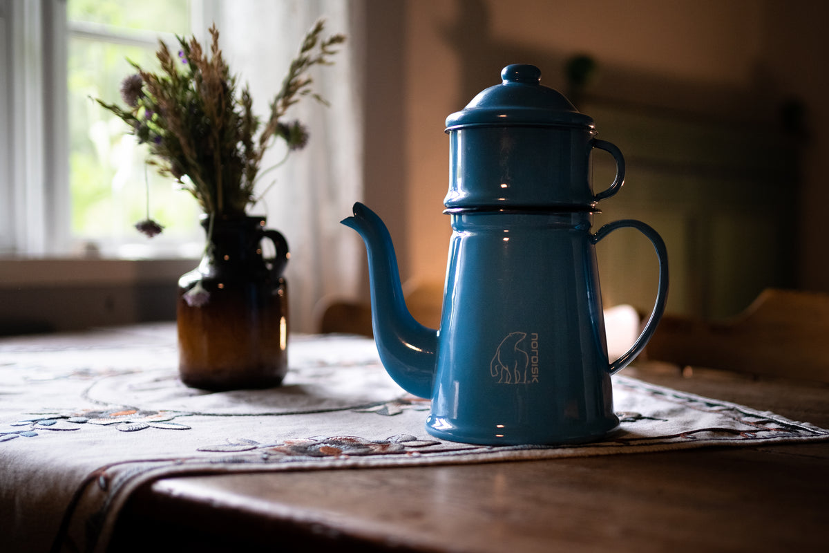 Blue Nordisk Madam Blå enamel coffee pot on a rustic table with flowers.