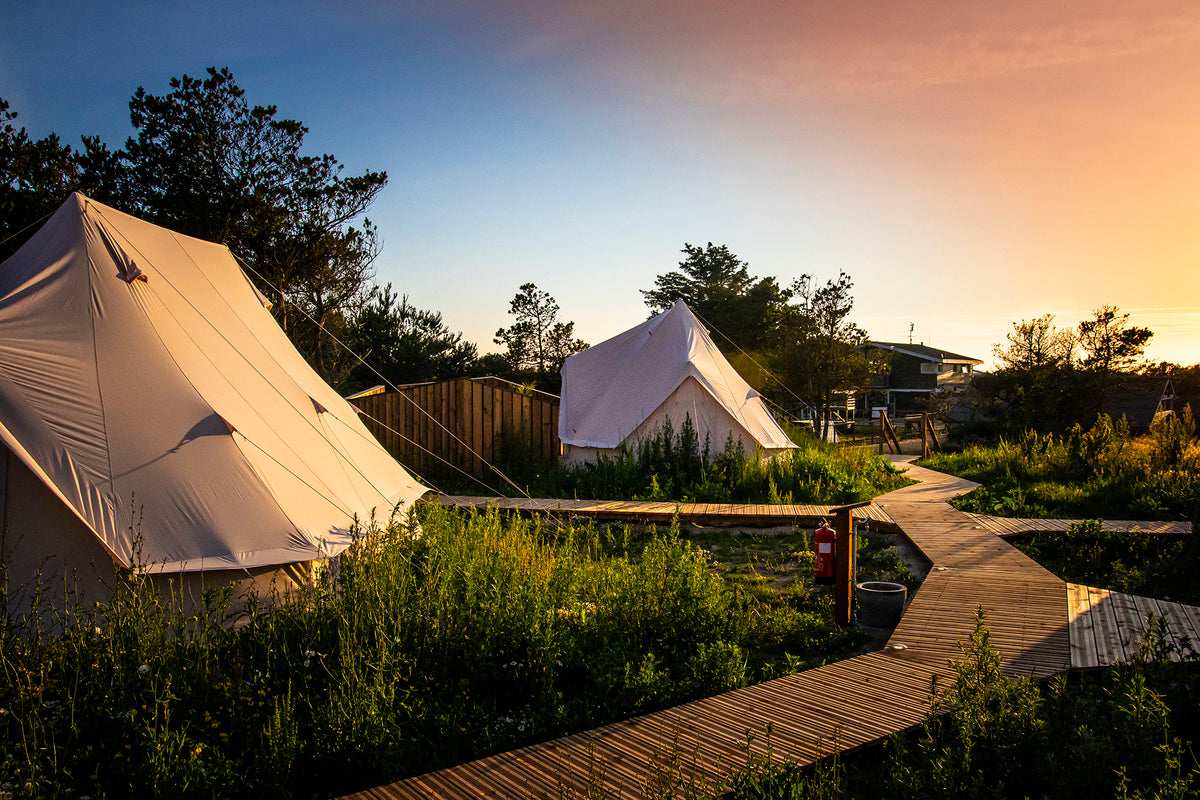 Luxury glamping cotton tents with a wooden boardwalk at sunset for a nature holiday experience.
