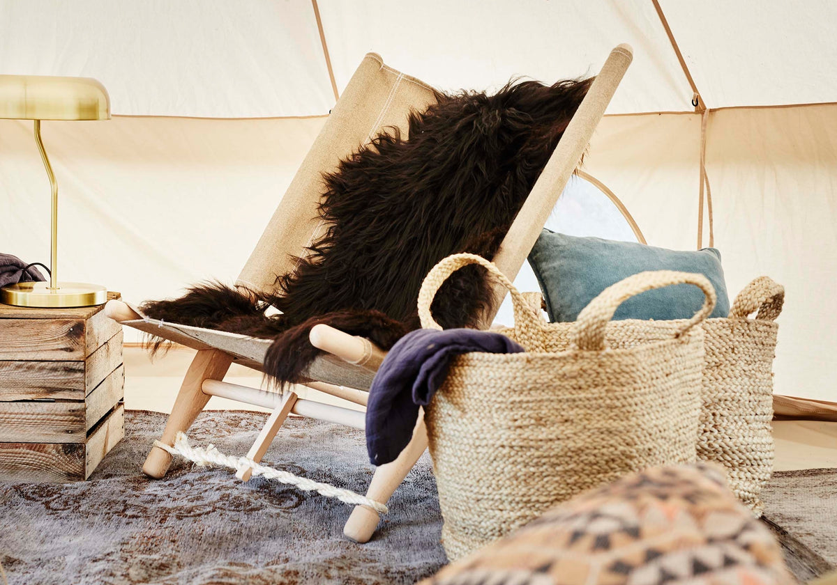 Luxurious glamping tent interior featuring a wooden lounge chair with faux fur and woven baskets.