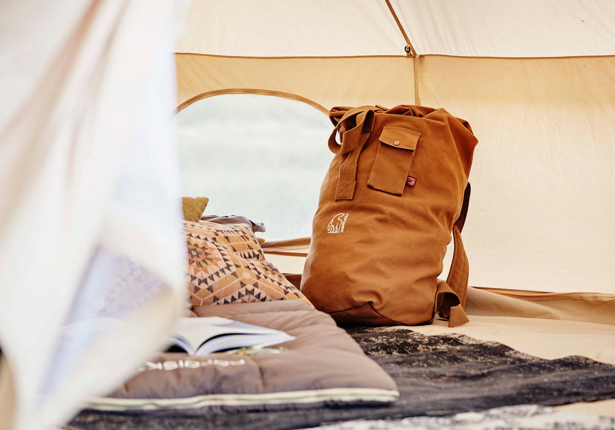 Interior of a Nordisk glamping tent with a bed, decorative cushions, and a canvas backpack.