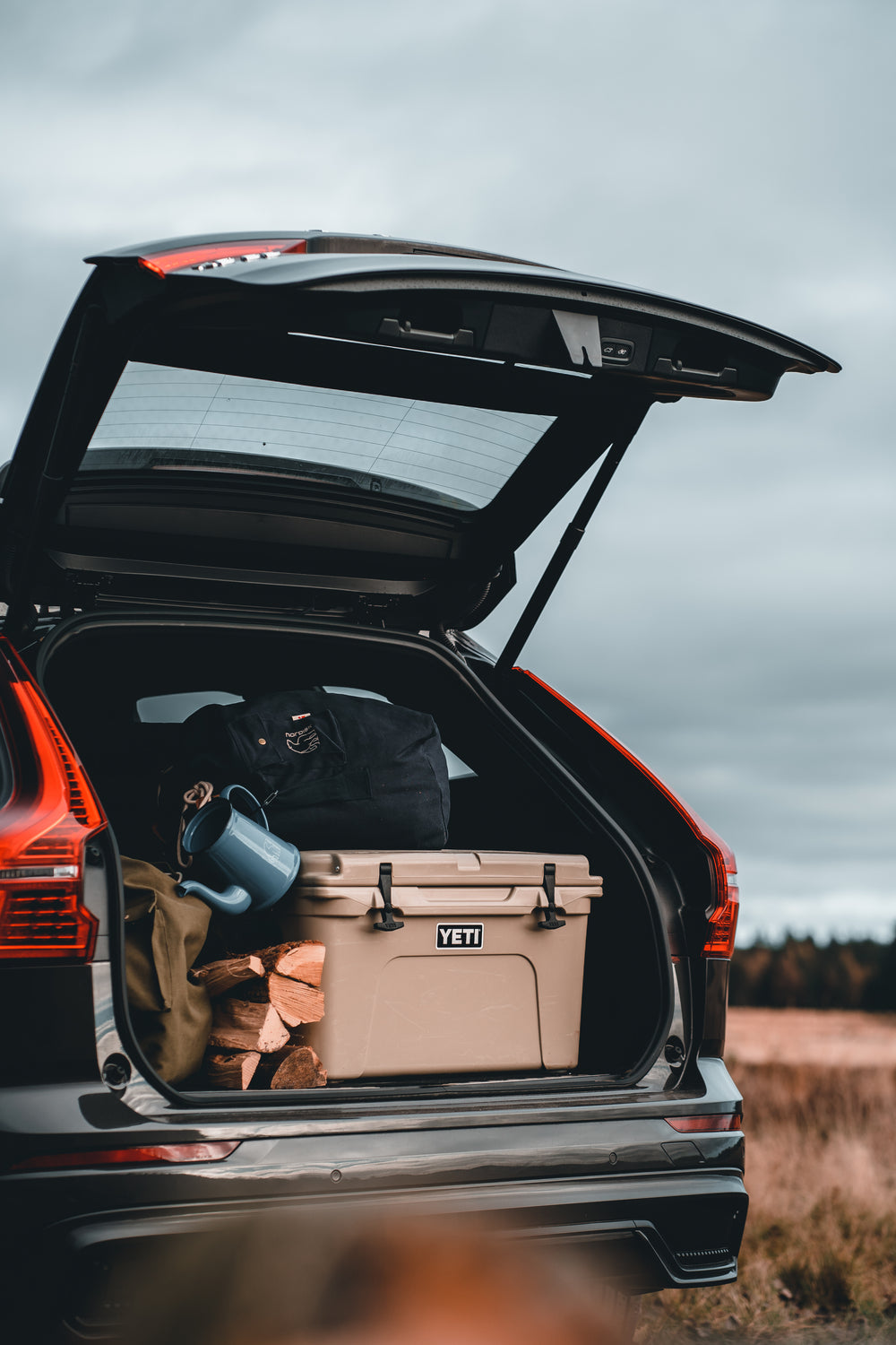 Outdoor glamping gear including a cooler, bag, and firewood packed into a car trunk.