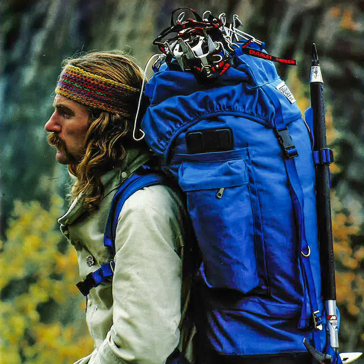Vintage outdoor explorer carrying a large blue Caravan backpack with climbing gear and ice axe.