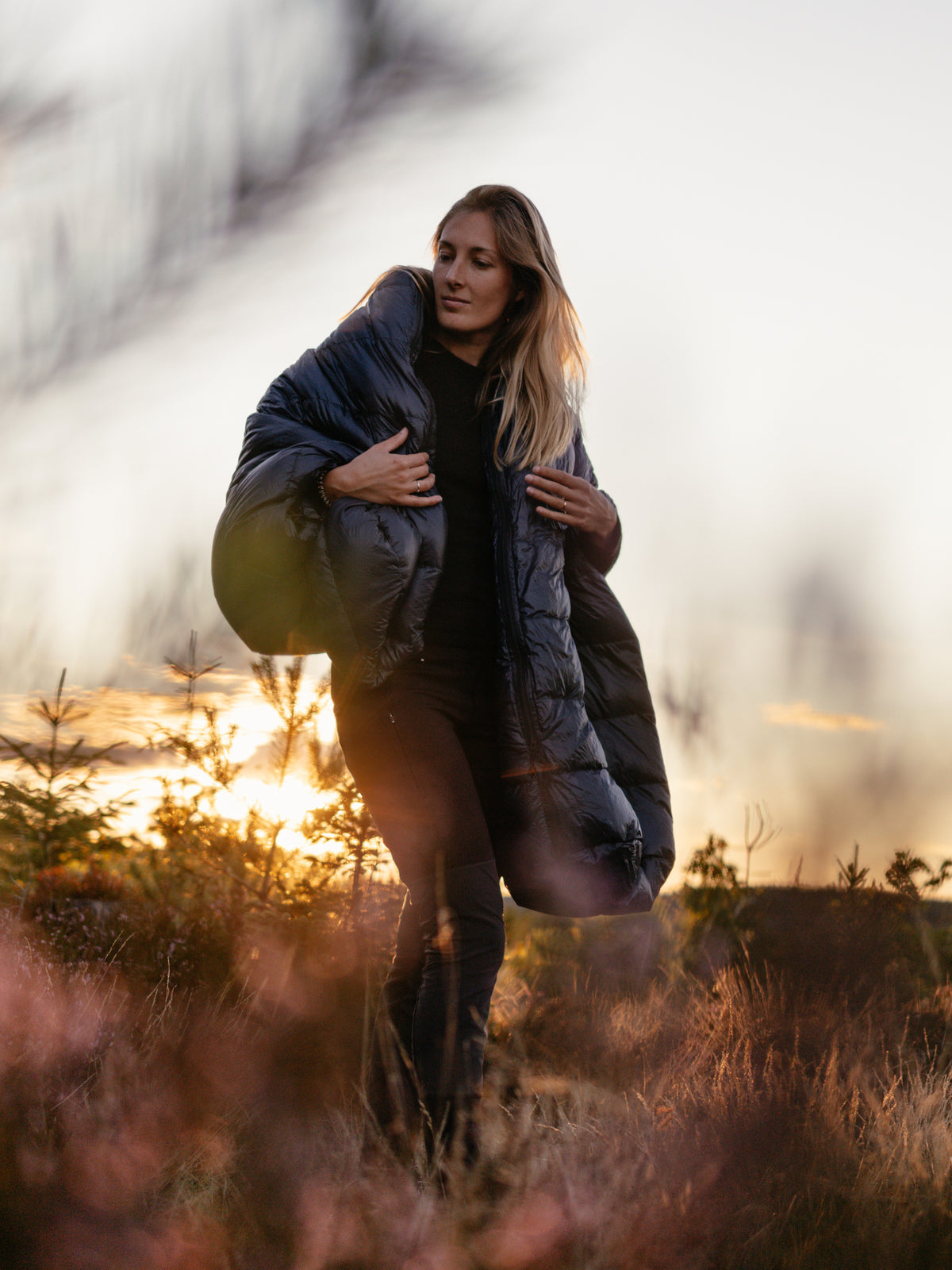 Franziska from Ins Nirgendwo wearing a Nordisk sleeping bag in the nature at sunset.