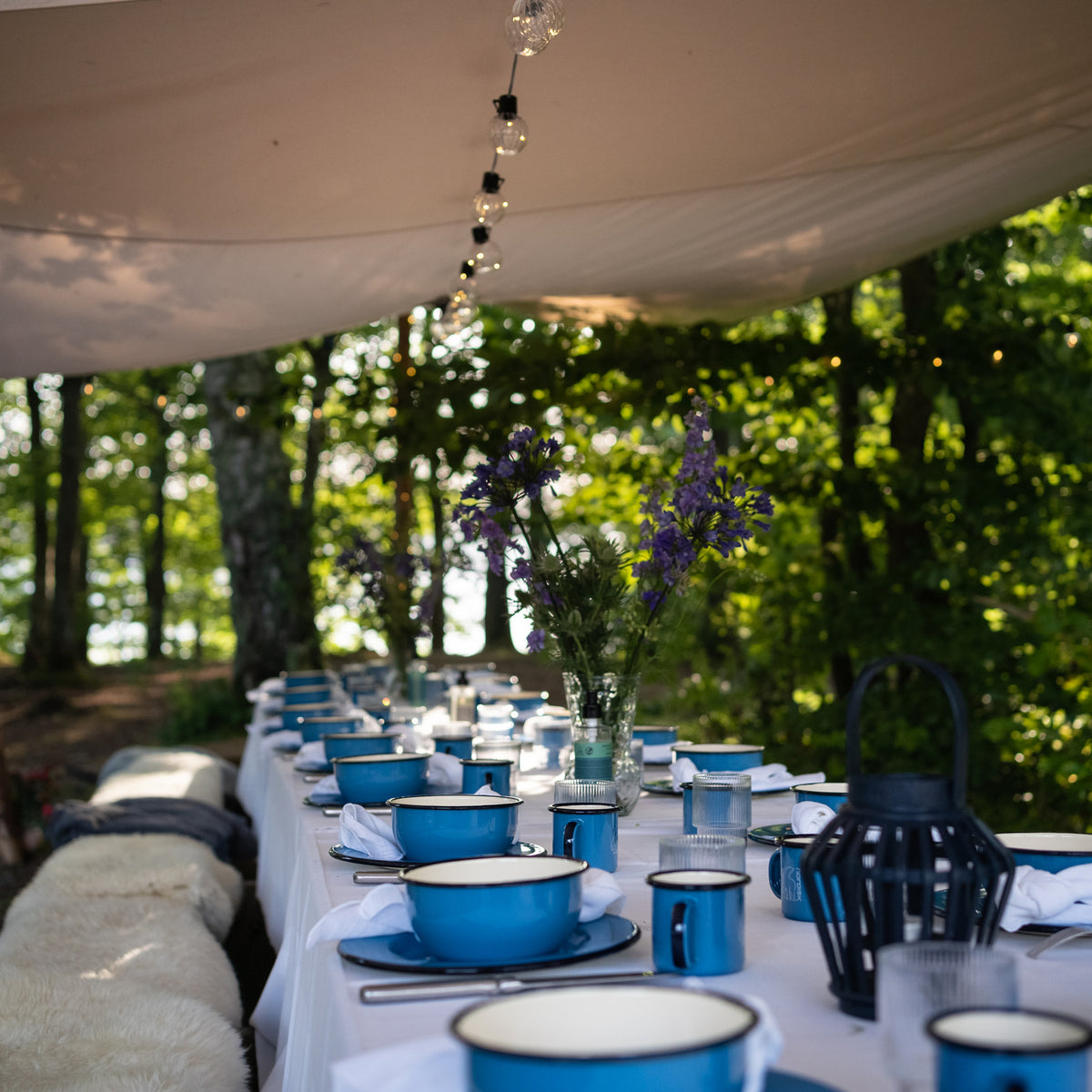 Outdoor dining table set with blue Madam Blå enamel bowls and cups for a Hygge moment.