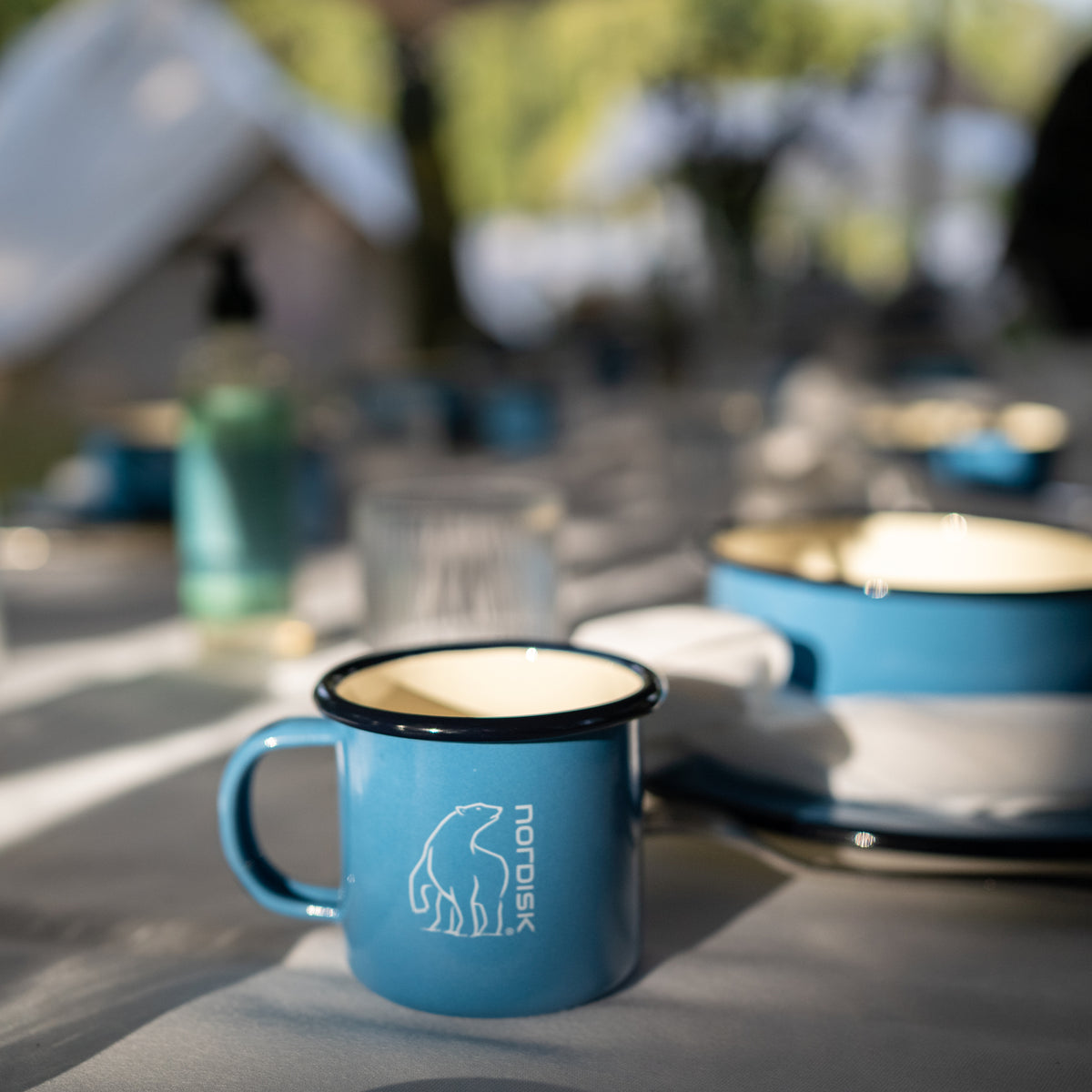 Sky blue Madam Blå enamel cup with Nordisk logo on an outdoor dining table.