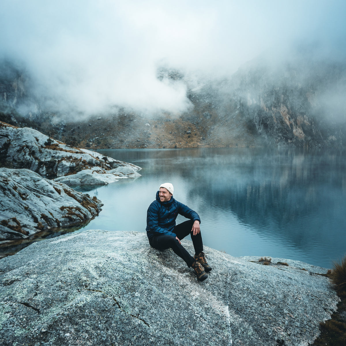 Maximilian Lehrke sitting on a rock overlooking a foggy mountain lake in Peru.