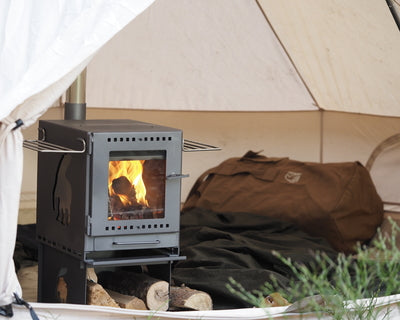 Portable Torden wood burner stove with burning logs inside a Nordisk cotton tent.
