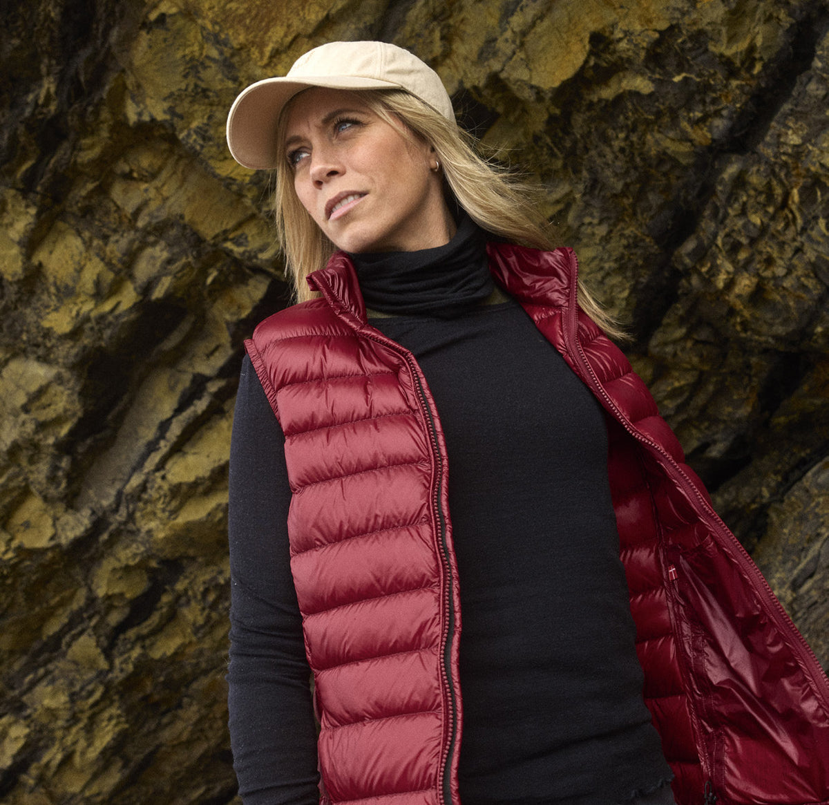 Woman wearing the Companyon Asta down vest in Tibetan Red in front of a rock face