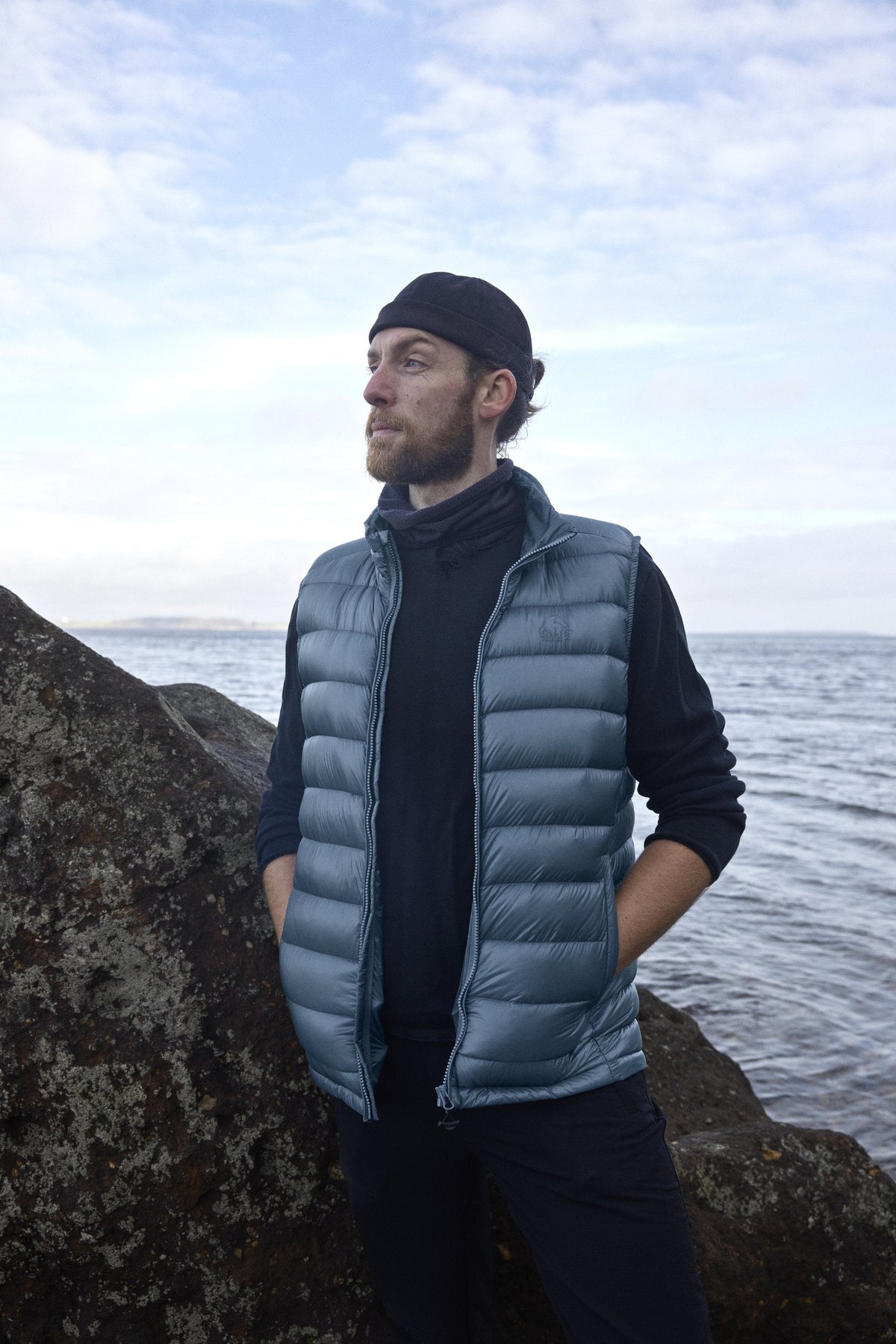 Man wearing the Companyon Harald down vest in Blue Mirage by the sea