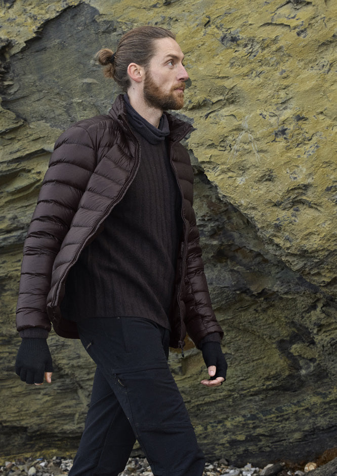 Man wearing the Companyon Hjalte down jacket in Black Coffee by a rock face