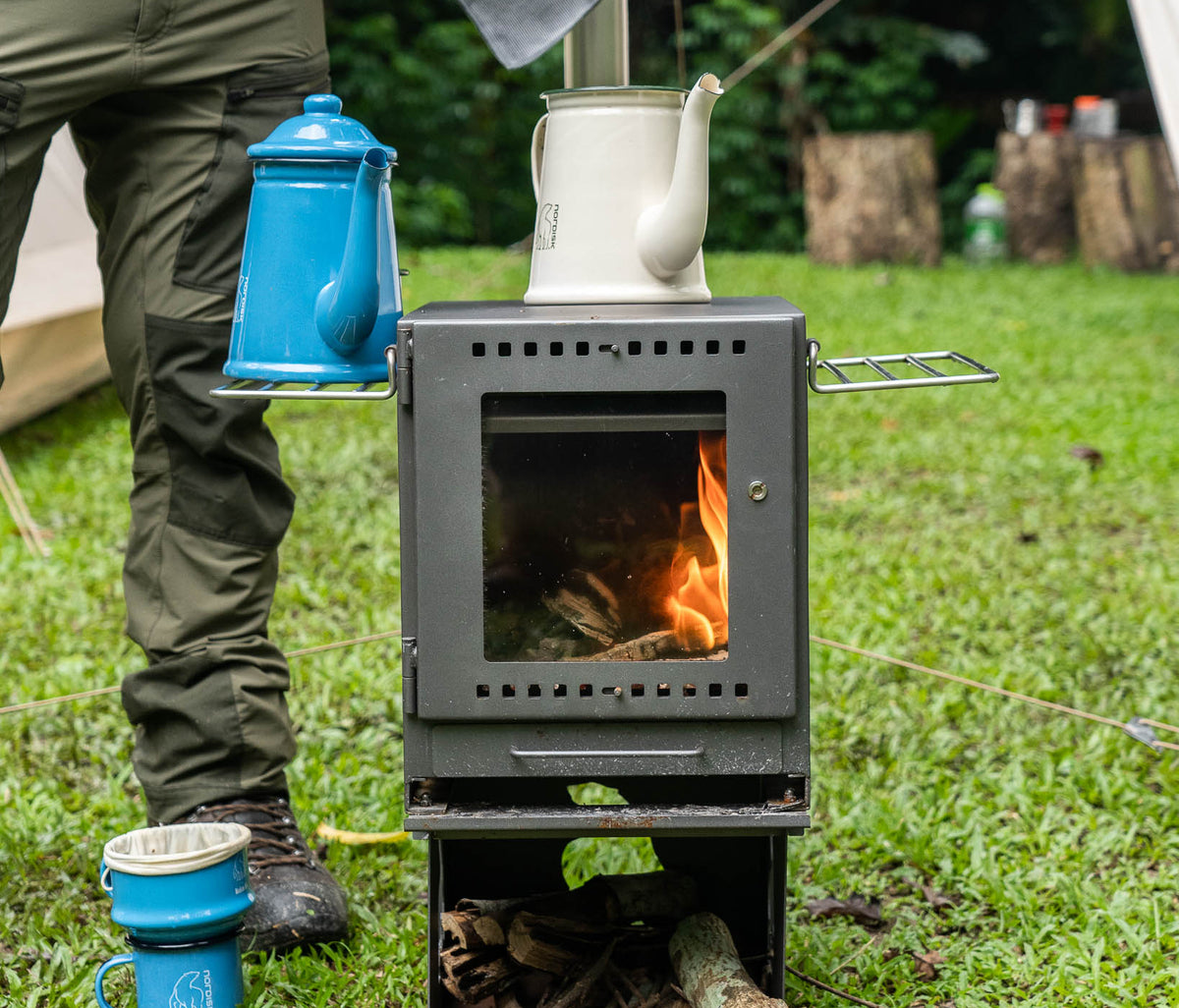 Madam Blå enamel coffee pots in sky blue and cream on a portable wood-burning camping stove.
