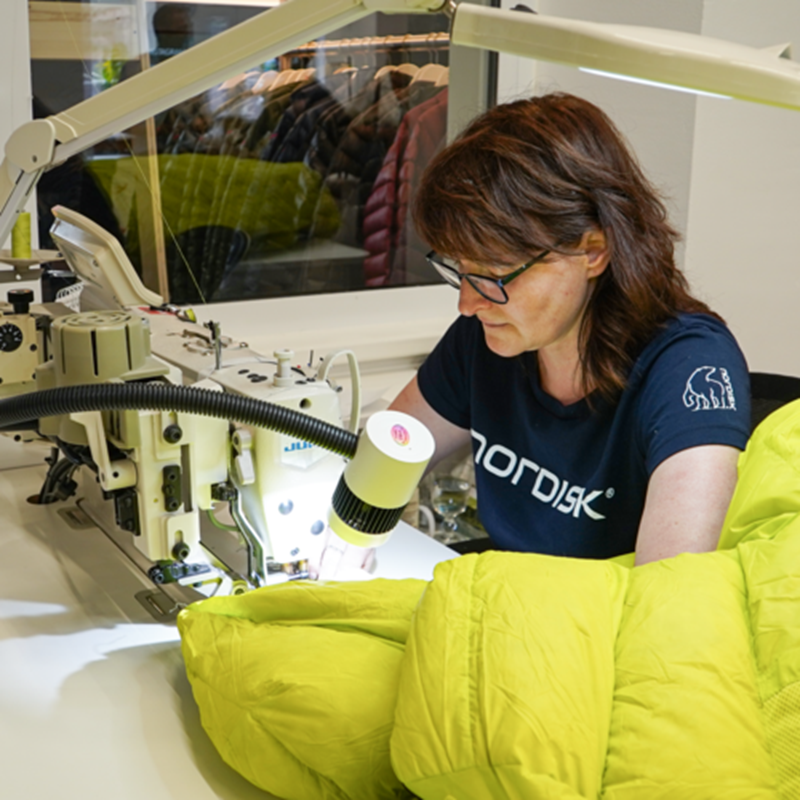 A woman at Nordisk Die Manufaktur in Germany sewing a bright yellow down jacket.