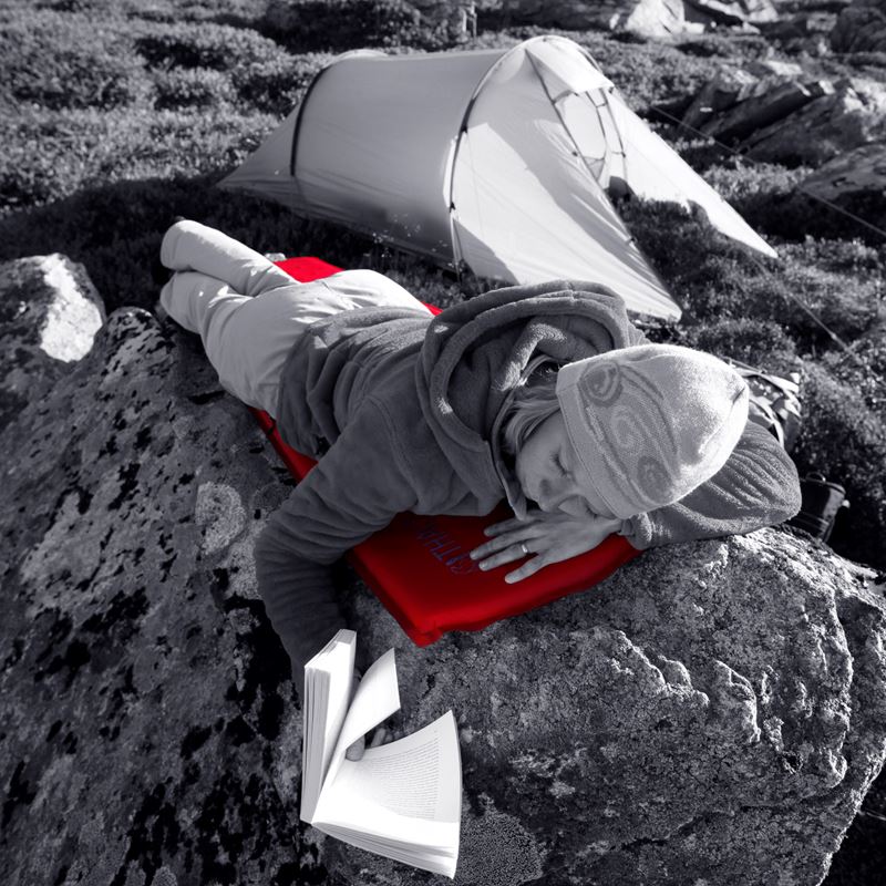 Woman resting on a red Nordisk sleeping mat next to a tent while camping.